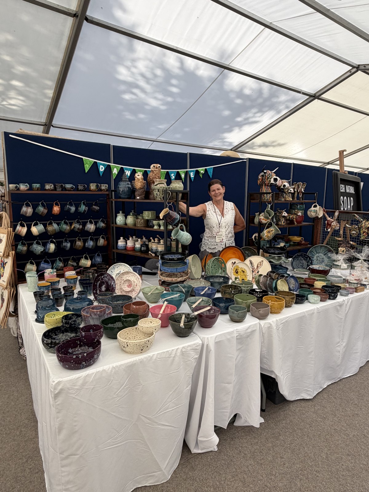 A smiling ceramic maker displaying handmade pottery at the Essex County Craft Show