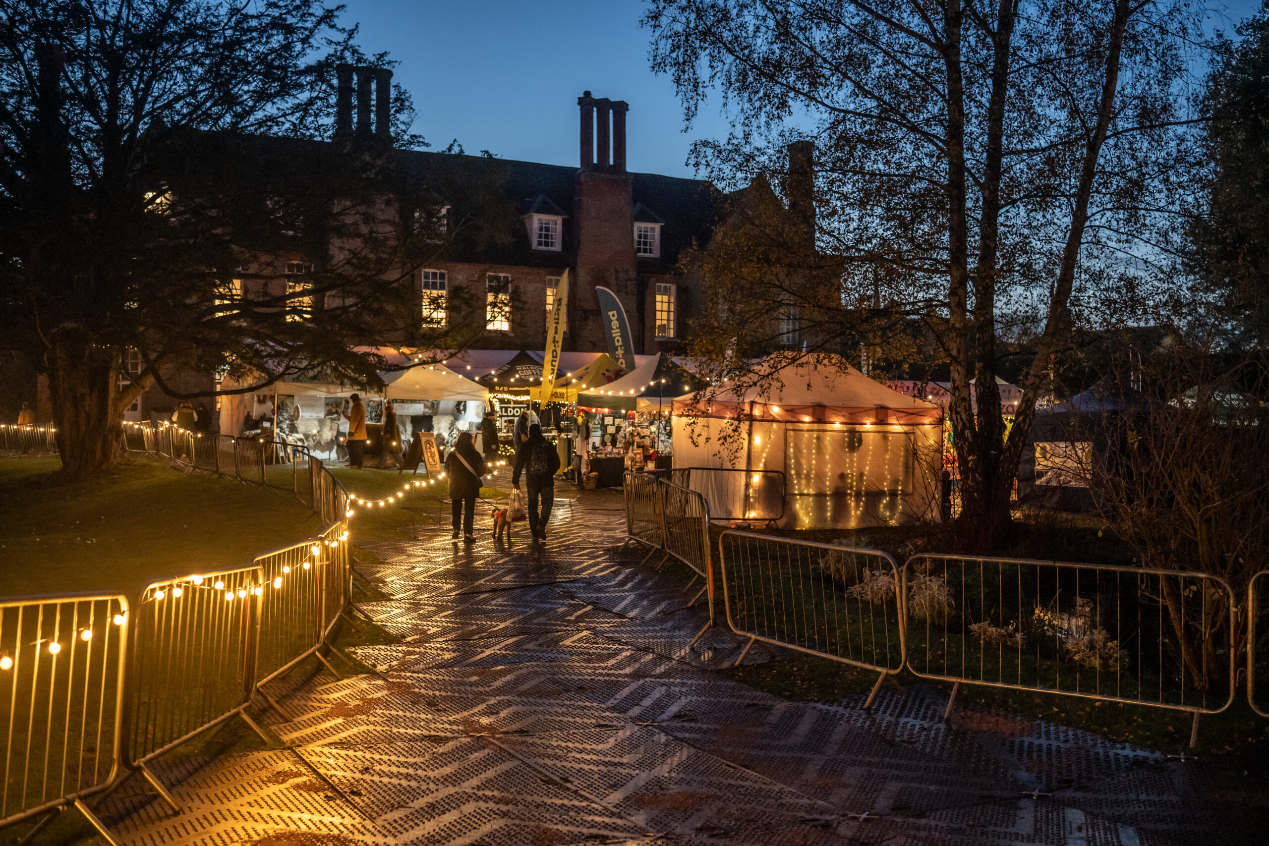 Visitors exploring illuminated stalls at Hintlesham Hall after dusk